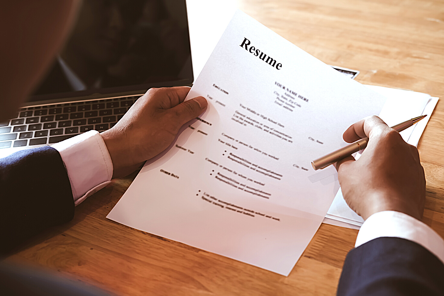 HR Manager Reviewing Resume Information on His Wooden Desk